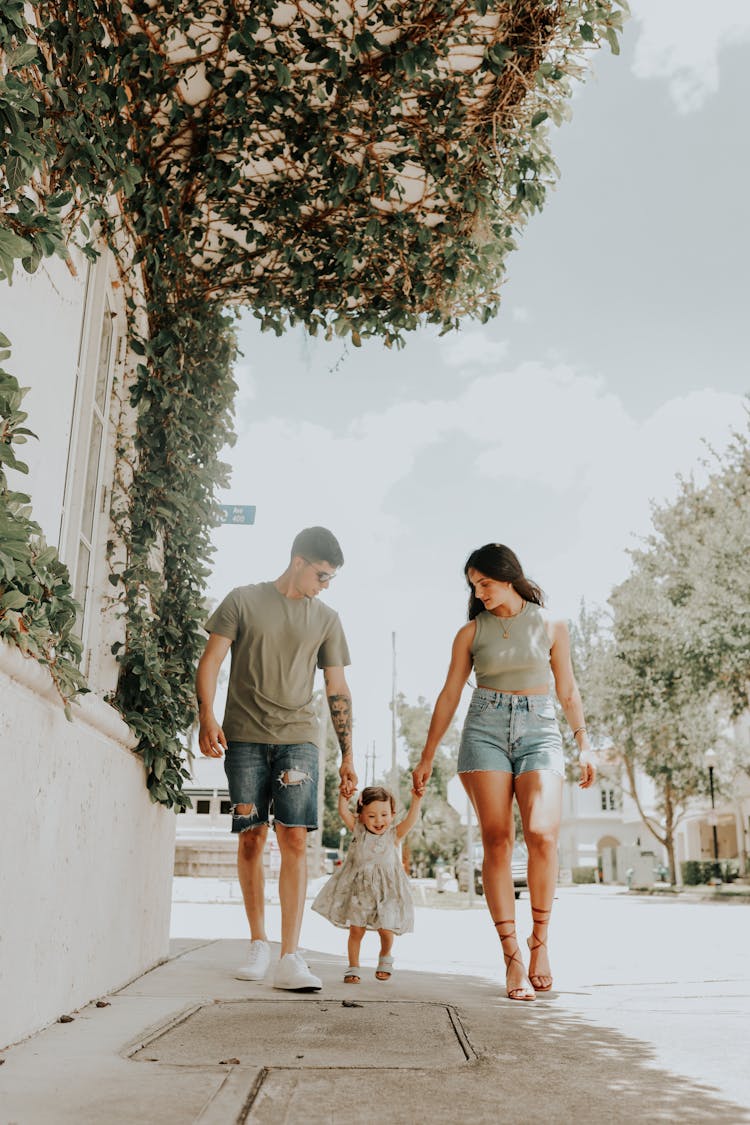 Parents With Daughter Walking On Sidewalk