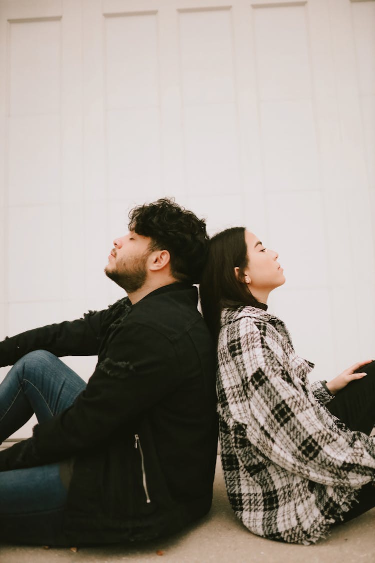 Man And A Woman Sitting On A Floor Back To Back