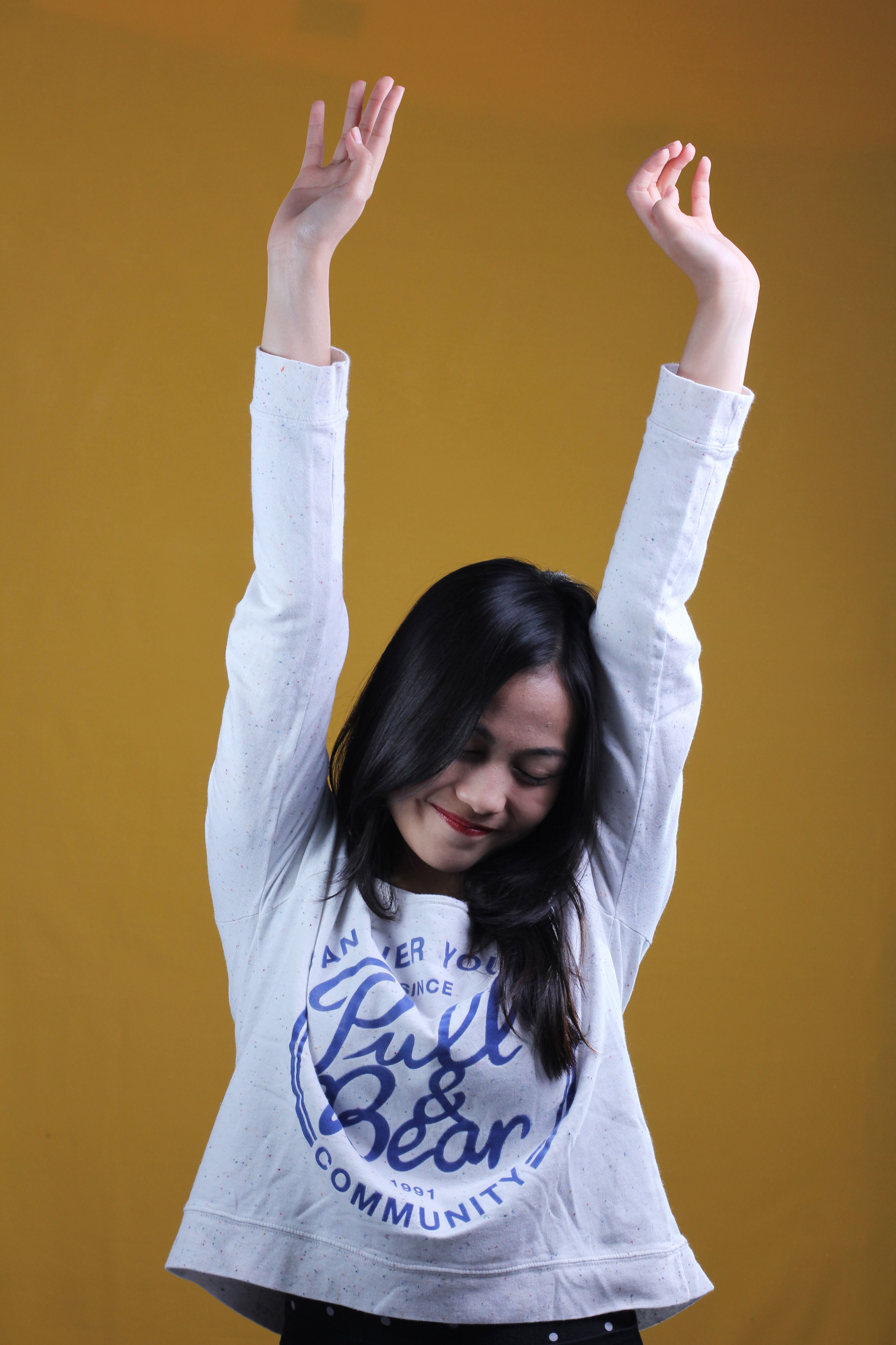 Smiling woman with arms raised in a cheerful pose against a vibrant yellow backdrop.