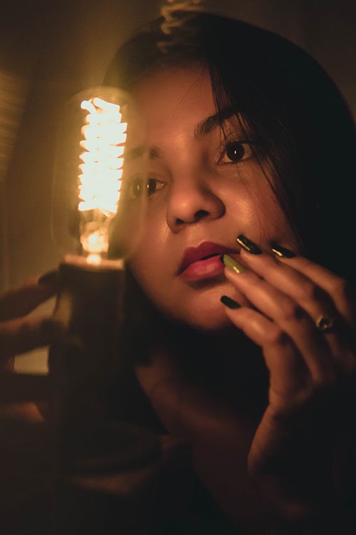 Free Close-up portrait of a woman with a glowing light bulb, creating a warm and moody ambiance. Stock Photo