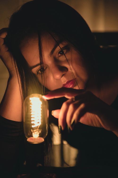 Free A woman interacts with a glowing vintage light bulb, creating a warm and mysterious ambiance. Stock Photo