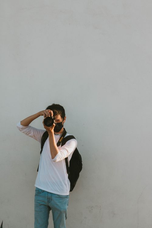 Free A young man taking a photograph against a plain white wall, offering clear copyspace. Stock Photo