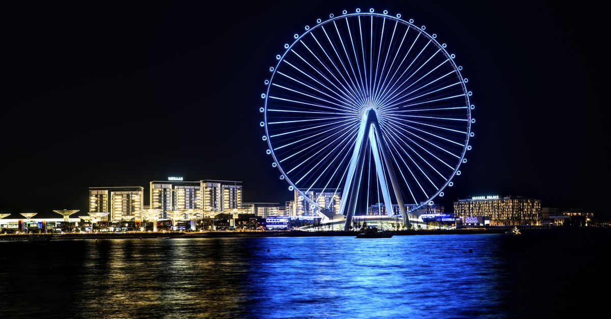 Stunning nighttime view of Dubai's Ferris wheel reflecting in the water, showcasing city lights.