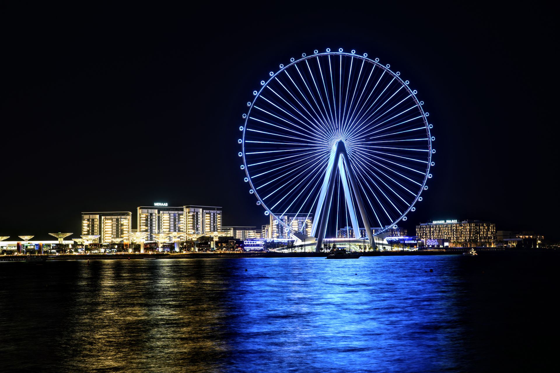 Stunning nighttime view of Dubai's Ferris wheel reflecting in the water, showcasing city lights.