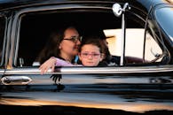 一对母女驾驶着一辆老式黑色汽车，在旅途中享受着家庭的宁静时光