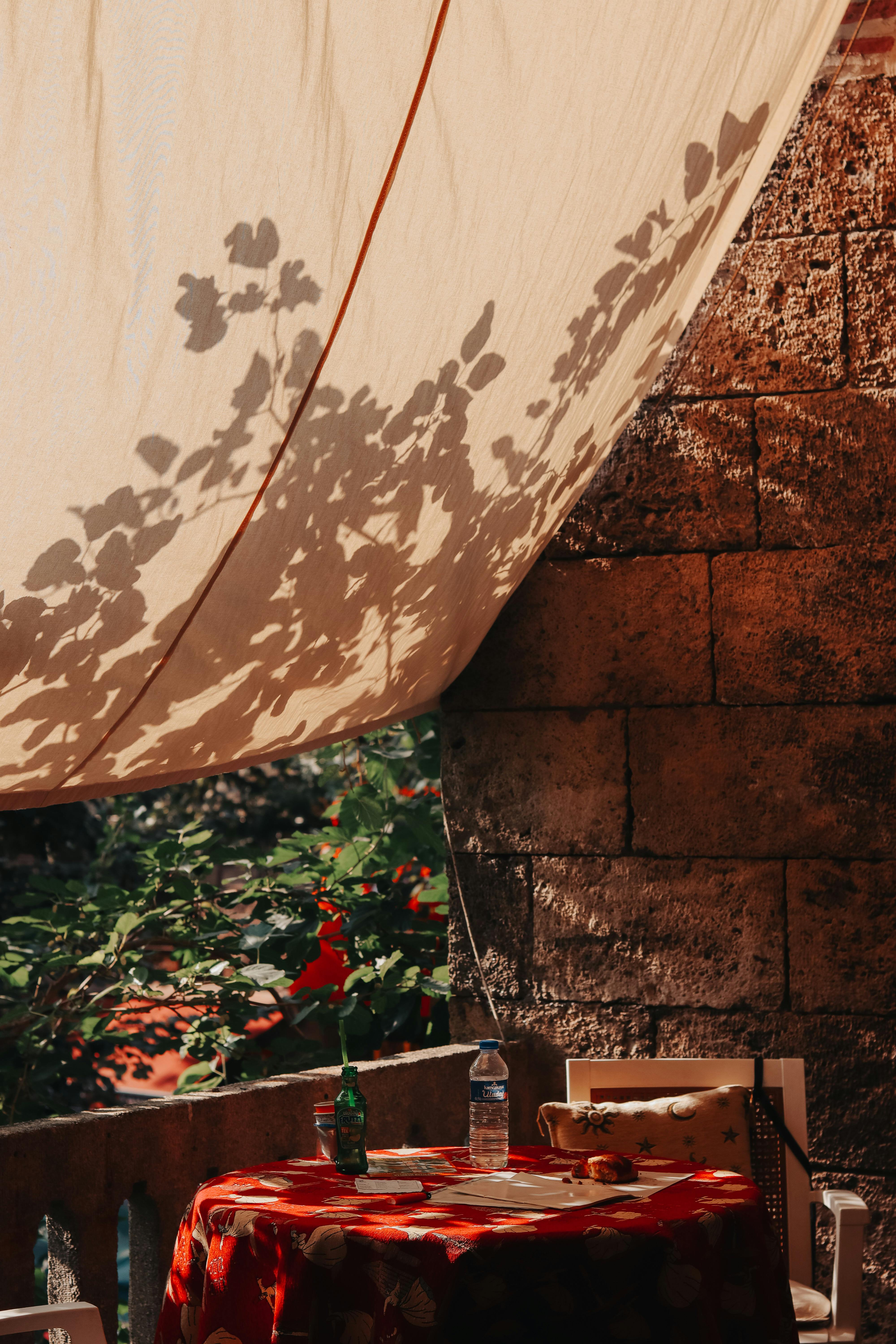 Relaxing outdoor patio with a sunlit fabric canopy casting leaf shadows, perfect for summer afternoons.