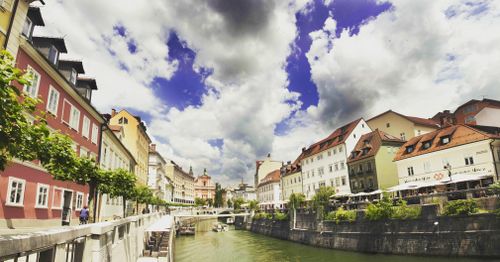 Free Scenic view of colorful riverside buildings in Ljubljana, showcasing vibrant architecture under dramatic skies. Stock Photo