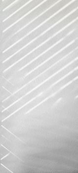 Minimalist photo of diagonal light patterns on a white textured wall, creating an abstract visual.