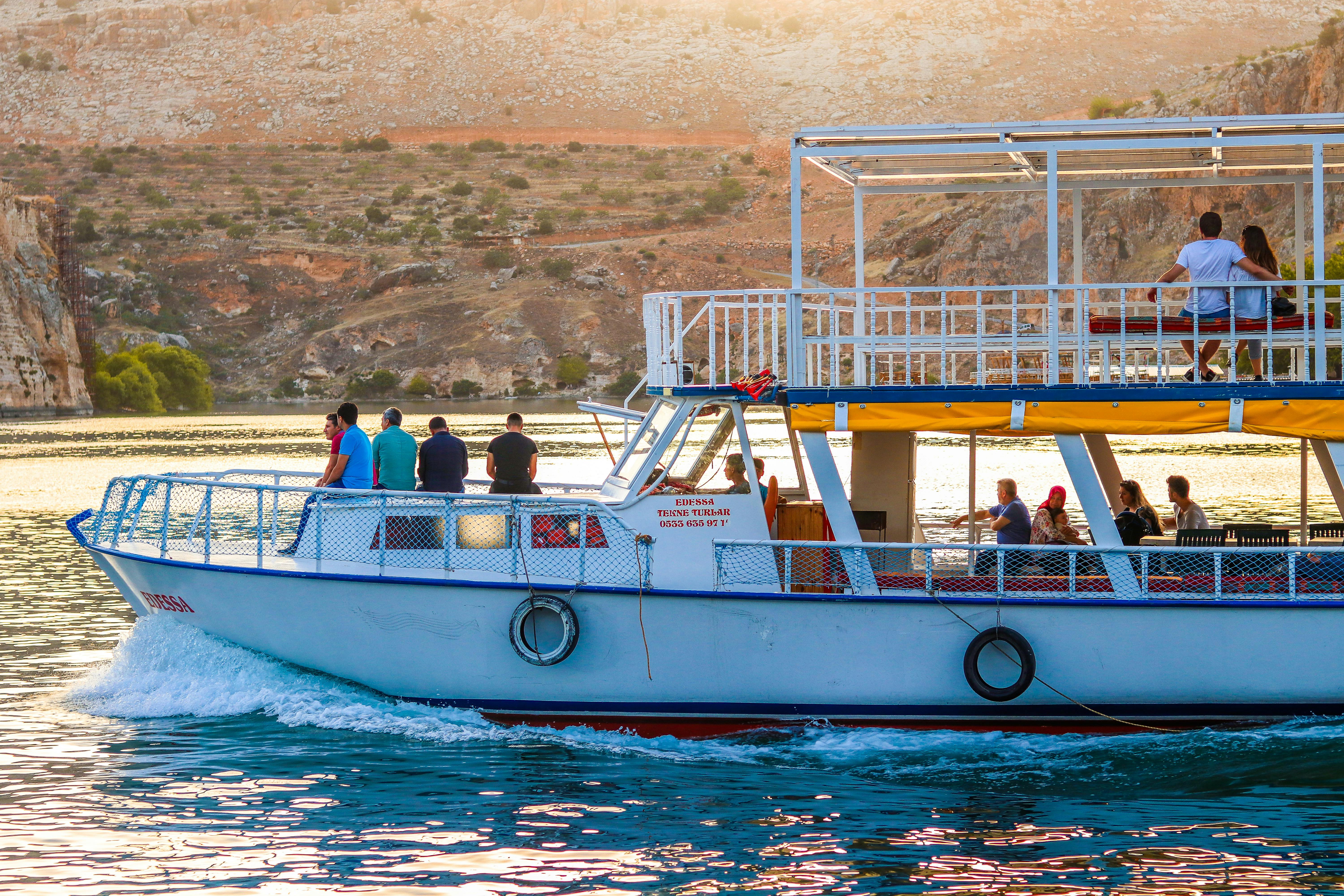 一艘载着乘客的船沿着风景秀丽的河流航行，背景是岩石山丘，人们享受着悠闲的体验