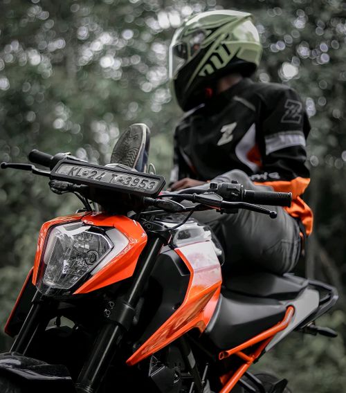 Free Person wearing helmet and gear on a vibrant orange motorcycle in a forest setting. Stock Photo