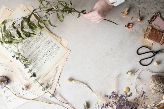 A creative flat lay featuring sheet music, dried flowers, and crafting materials on a white background.
