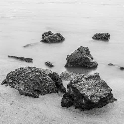 Grayscale Photo of Rocks on the Shore 