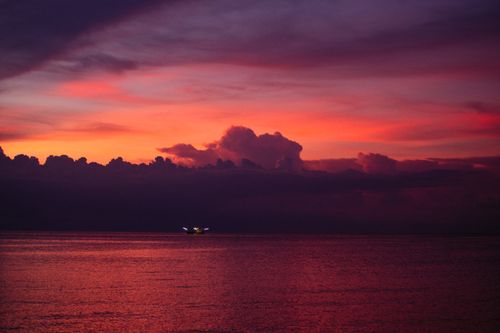 Free A breathtaking view of a dramatic sunset with vivid colors over the tranquil ocean, with a small boat in the distance. Stock Photo