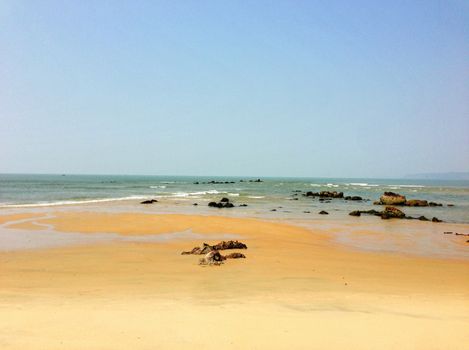 Serene coastal view with rocks and calm ocean waves under a clear blue sky.