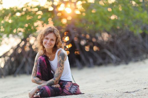Free Caucasian woman with tattoos sitting on a sandy beach, enjoying the sunset. Stock Photo