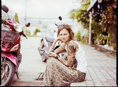 Free A tattooed woman in a white tank top and skirt sitting beside motorcycles outdoors. Stock Photo