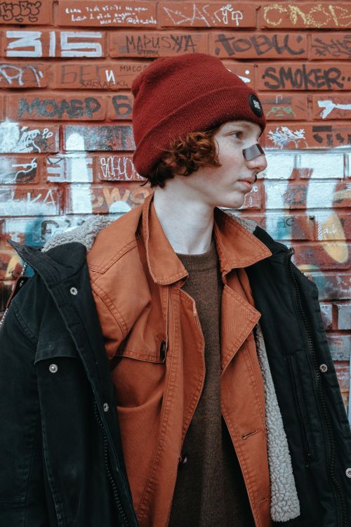 Free Teen wearing red knit hat and jacket against graffiti wall, showcasing urban street fashion. Stock Photo