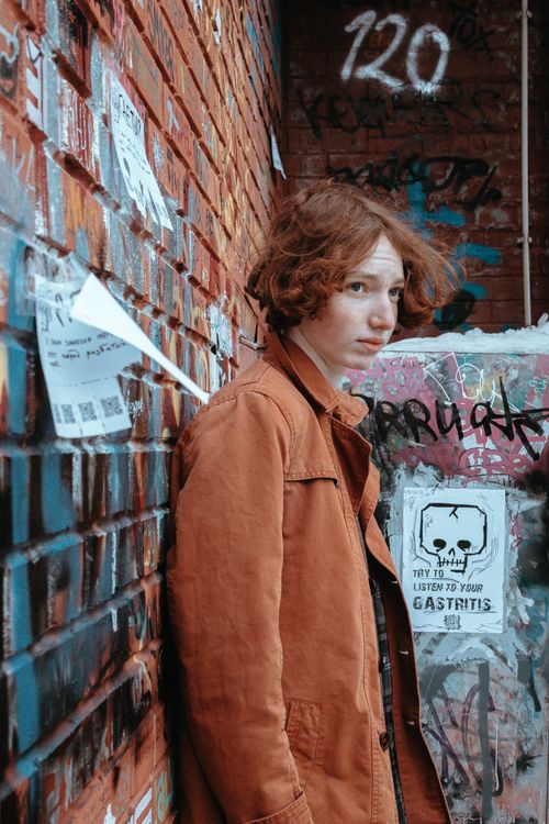 Free Portrait of a teenage redhead boy standing beside an urban graffiti wall. Stock Photo