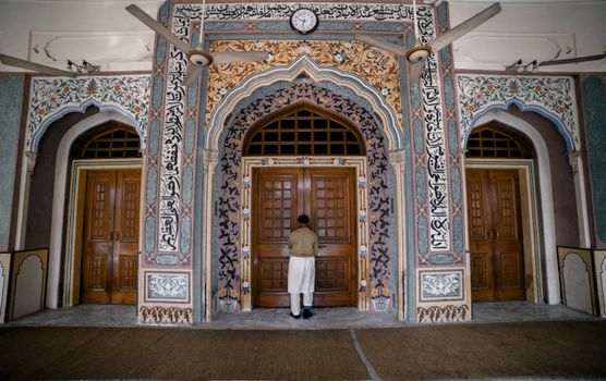 A man stands before an ornate mosque entrance in Faisalabad, showcasing Islamic architecture.