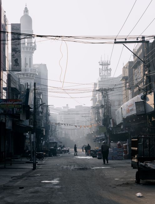 Busy urban street in Faisalabad with buildings, electric wires, and people walking.