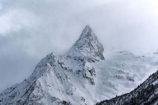 Captivating view of a snow-covered mountain peak in Dombay, Russia, set against a cloudy sky.