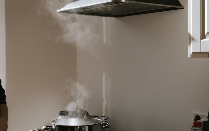 Sunlight illuminates a modern kitchen with steam rising from pots under a range hood.