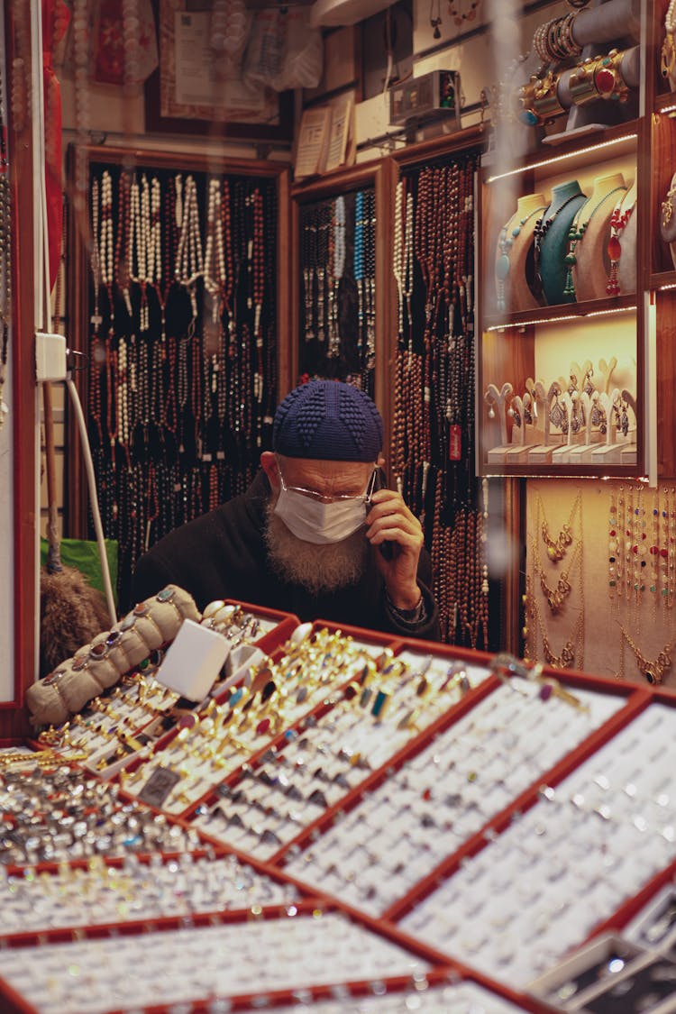 Salesman In Jewellery Shop Sitting At Counter And Talking On Mobile Phone