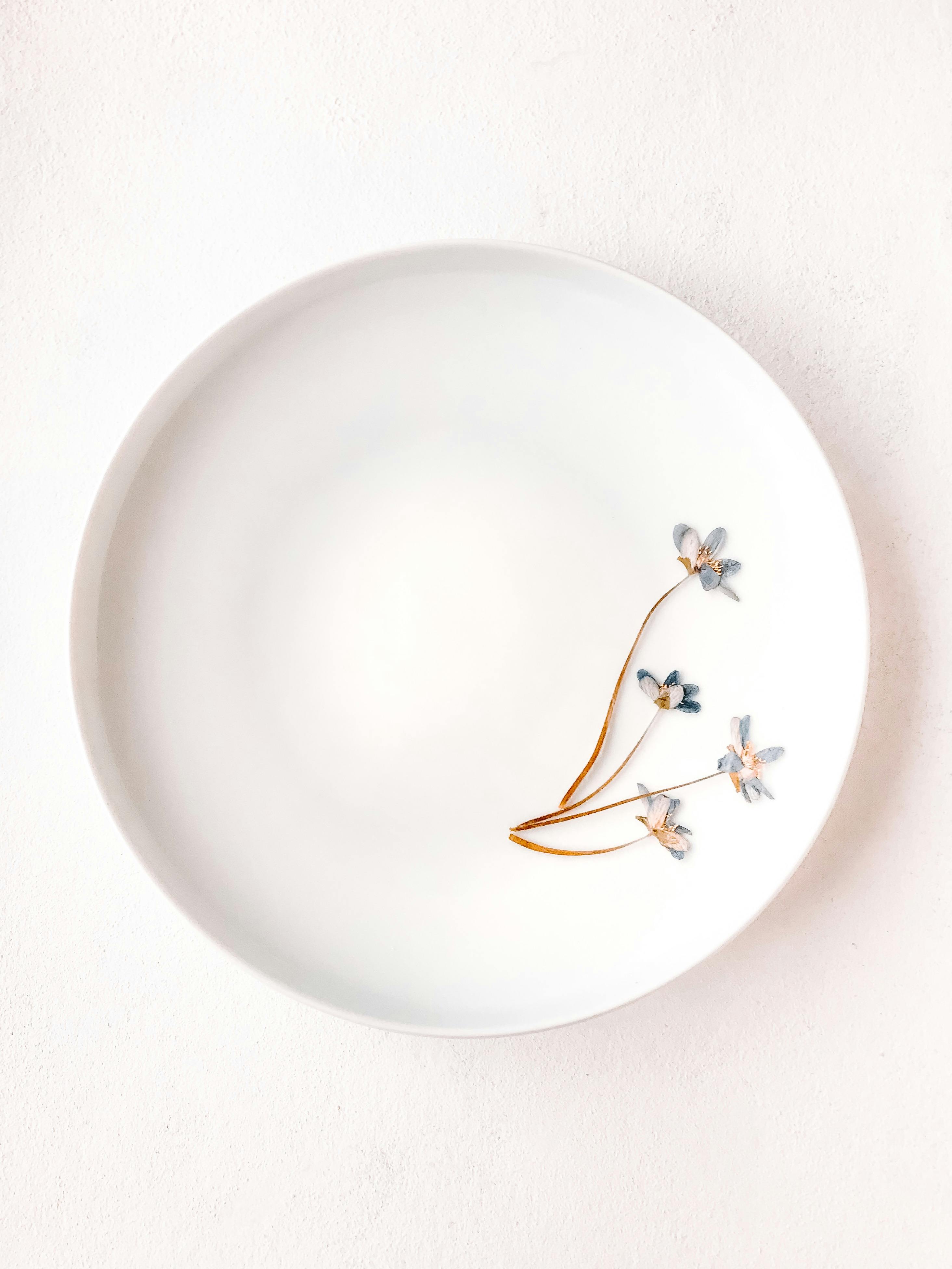 A minimalist white plate featuring three delicate dried flowers on a pristine white background.