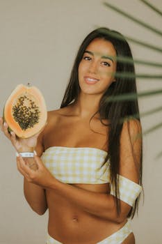 Smiling woman holding papaya in a bikini, promoting natural skincare benefits.