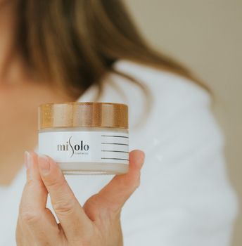 Close-up of a hand holding Misolo facial cream jar isolated on neutral background.
