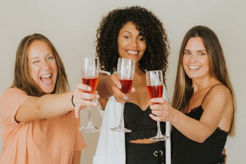 Women Holding Glasses with Red Wine while Smiling at the Camera
