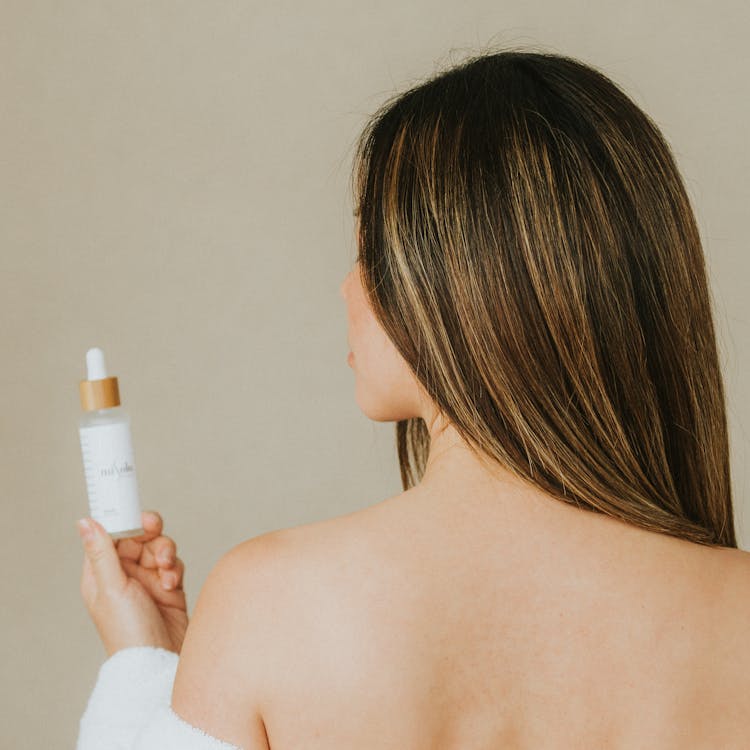 Back View Shot Of A Woman Holding A Serum Bottle