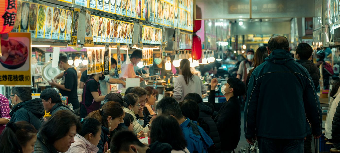 Busy food court with diners and multiple stalls — shared drains, bins and ceiling voids make pest control a centre-wide problem