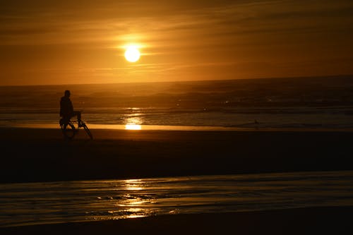 
A Silhouette of a Person Sitting on a Bicycle on a Shore during the Golden Hour