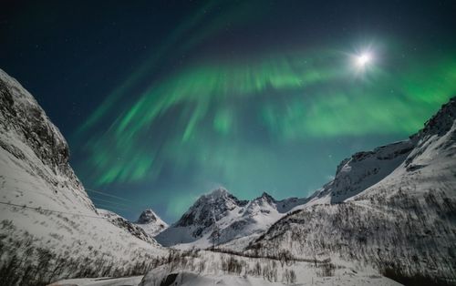 Free Captivating view of the Northern Lights dancing over snow-covered mountains under a moonlit sky. Stock Photo