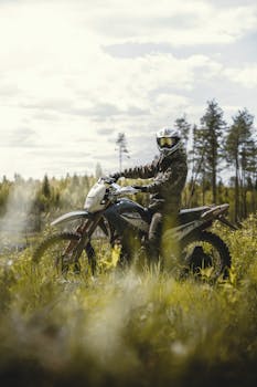 Motorcyclist riding dirt bike through grassy terrain on a sunny day outdoors.