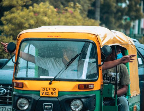 Free Auto rickshaw navigating the rainy streets of Delhi with passengers gesturing directions. Stock Photo