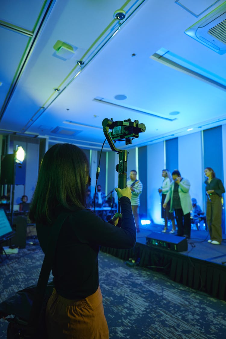 Woman Filming People On Stage In A Blue Lit Room