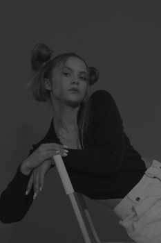 Elegant monochrome portrait of a woman with hair buns, leaning back elegantly on a chair.