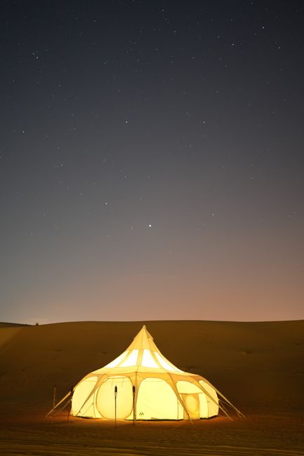 A glowing glamping tent set against a starry night sky in the Dubai desert.