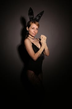 A stylish woman wearing a black bodysuit and bunny ears in a studio setting.