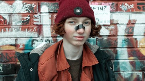 Free Young man in a beanie and jacket standing in front of a graffiti wall. Stock Photo