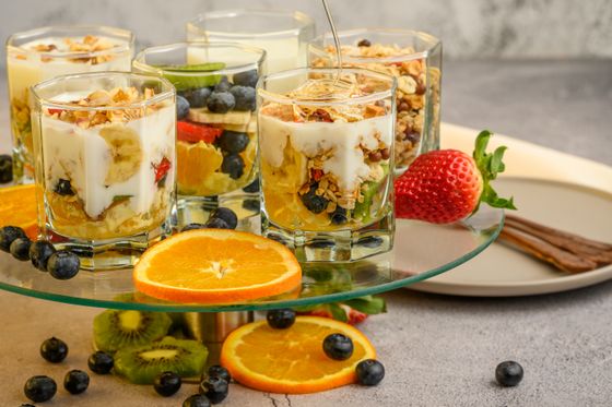 Glass tumblers layered with yogurt, granola, banana, blueberries and orange on a glass stand