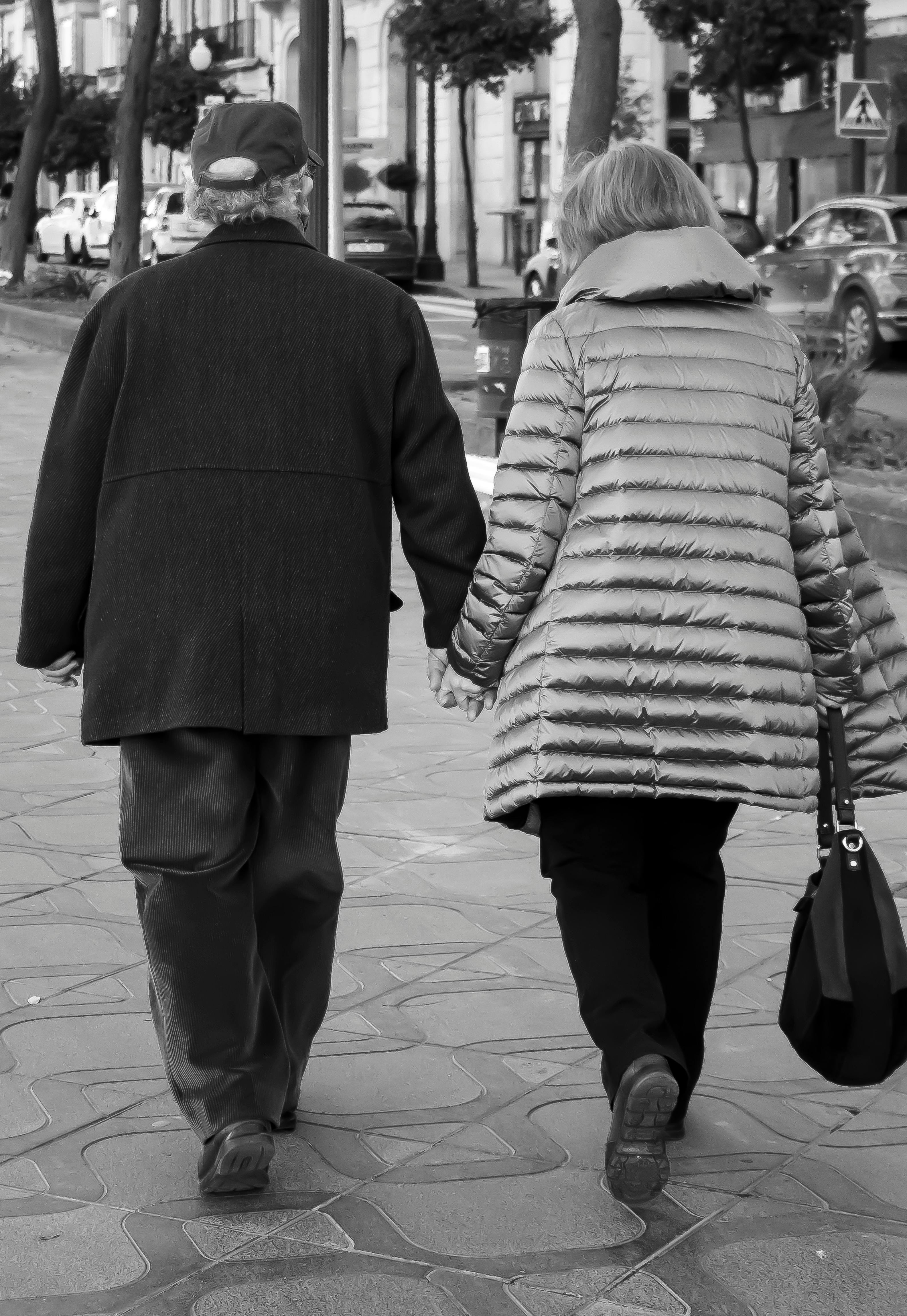 couple holding hands while walking on sidewalk