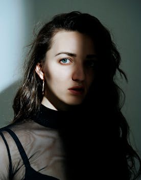 Artistic portrait of a woman with striking blue eyes in dramatic shadow and light.