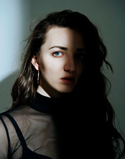 Artistic portrait of a woman with striking blue eyes in dramatic shadow and light.