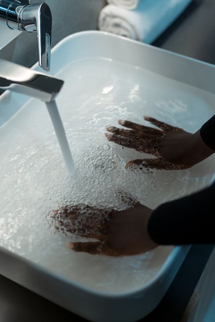 Hands submerged in water under a chrome faucet in a modern sink. Clean and refreshing.
