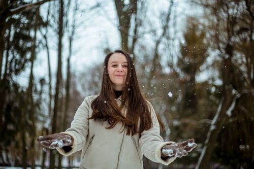 Free Cheerful woman in winter coat catching snowflakes in a snowy forest setting. Stock Photo