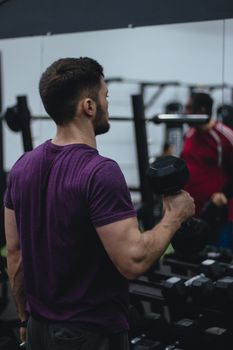 Side view of a man in a purple shirt lifting a dumbbell in the gym, focusing on strength training.