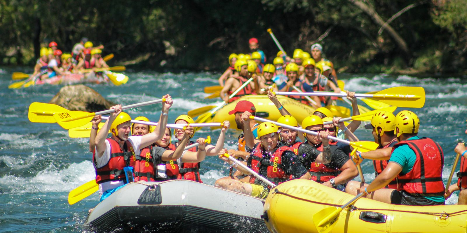 Teams of rafters navigating rapids in colorful inflatable boats